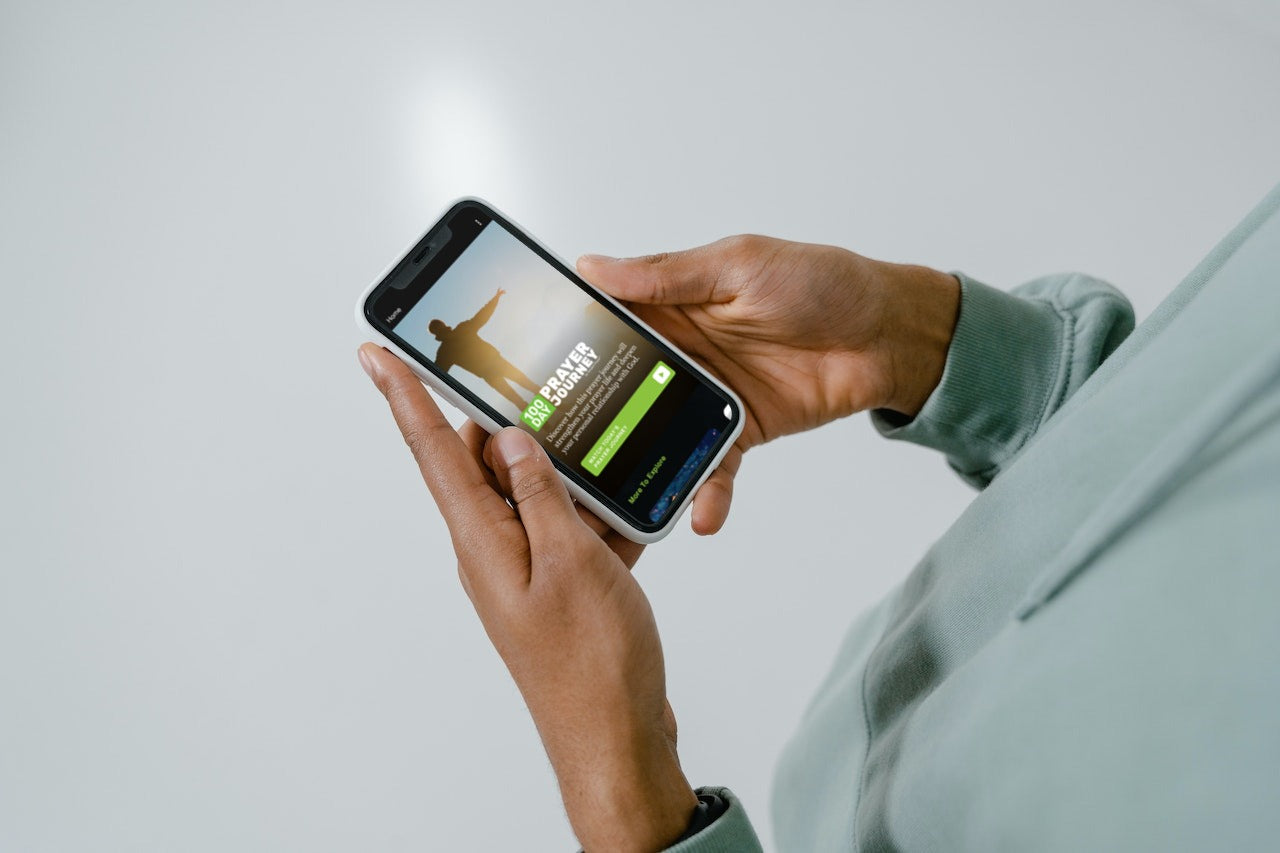 man holding a mobile phone showing the homepage of a prayer app
